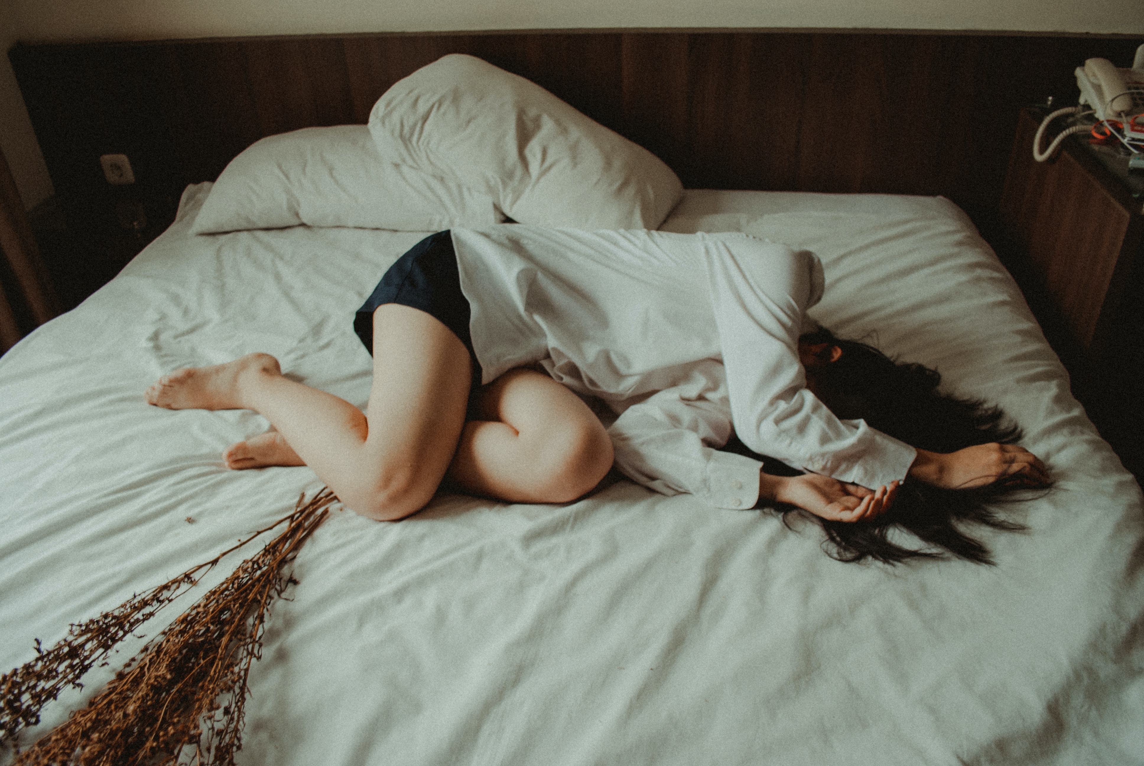 Mujer joven durmiendo en una cama destendida, se tapa el rostro con los brazos